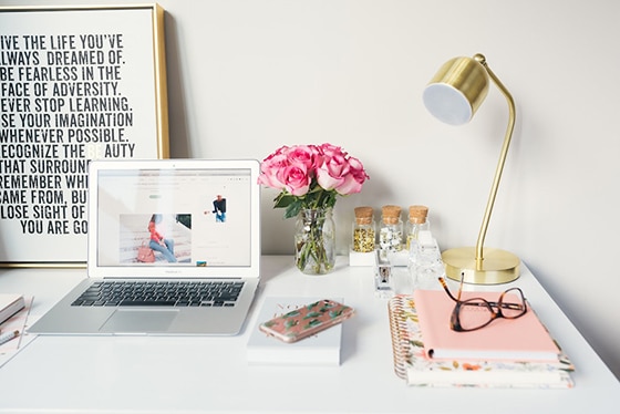 Desk with laptop, flowers, journals, a lamp and glasses