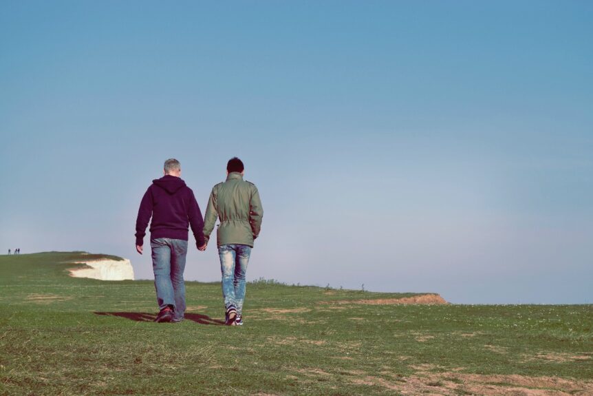 A gay couple in the LGBTQIA2+ community walking through a field and holding hands.