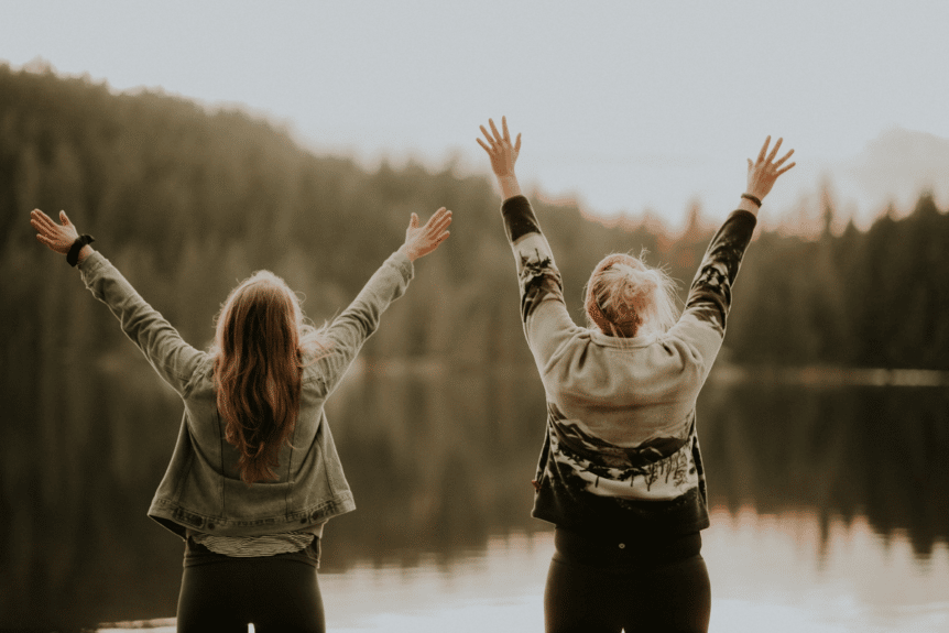 Two girls throwing their hands up in front of a lake, hosted by Wellin5 in Vancouver, BC